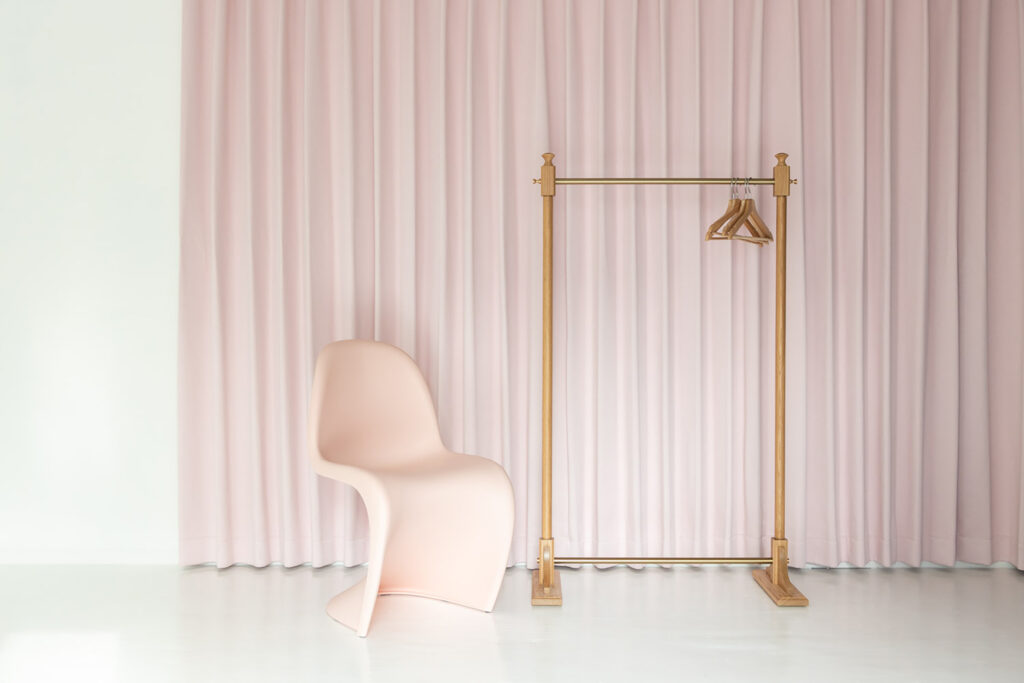 ピンクのカーテンの前にピンクの椅子とハンガーラックが並んでいます