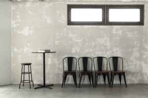 モルタル風の壁面前に並ぶ、ハイテーブル・ハイチェアと４脚の椅子