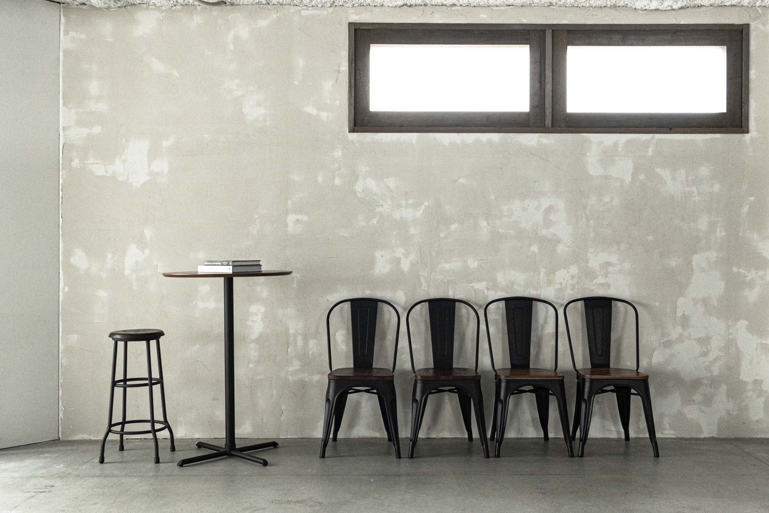 モルタル風の壁面前に配置されたテーブルセットと４脚の椅子