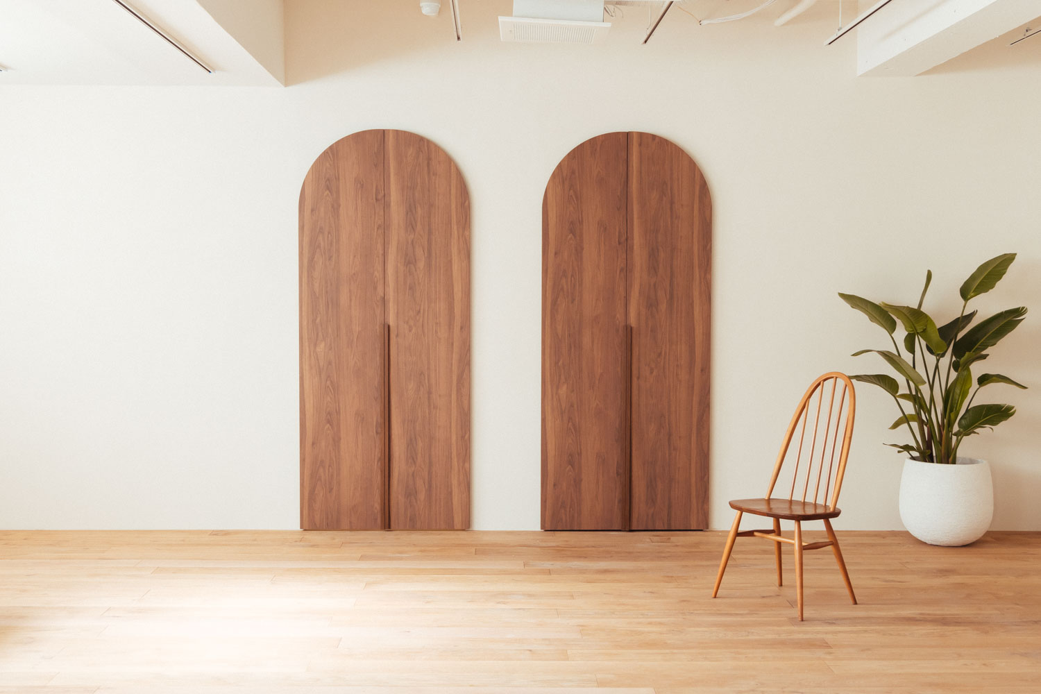 円形の木製ドア2枚があるフローリングの部屋に、アーコールチェアと観葉植物が配置された写真