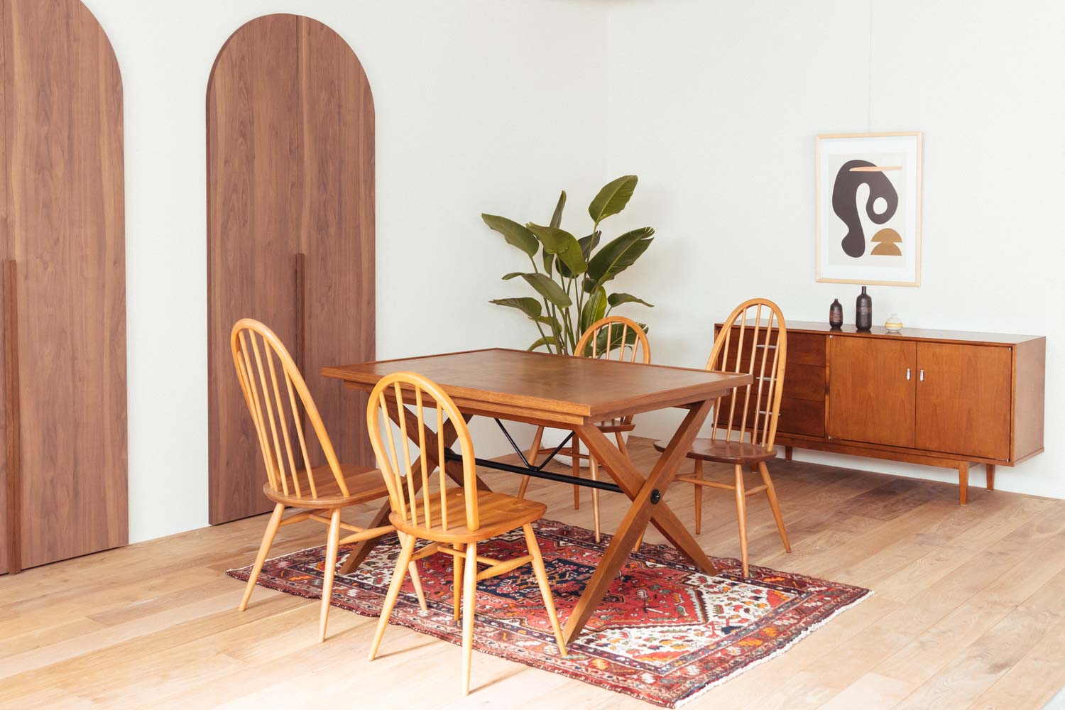 円形の木製ドアがあるフローリングの部屋に、木製テーブルと椅子4脚、観葉植物、チェストが配置された写真