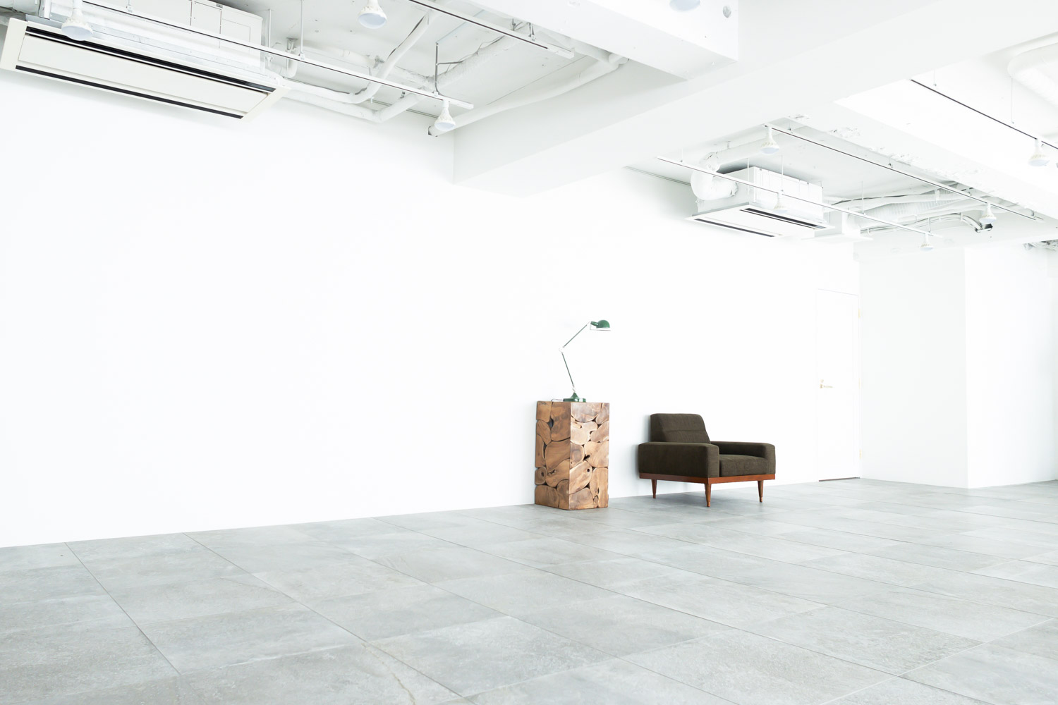 石の床タイルのスタジオに、木製スツールと一人掛けソファが並んでいる写真