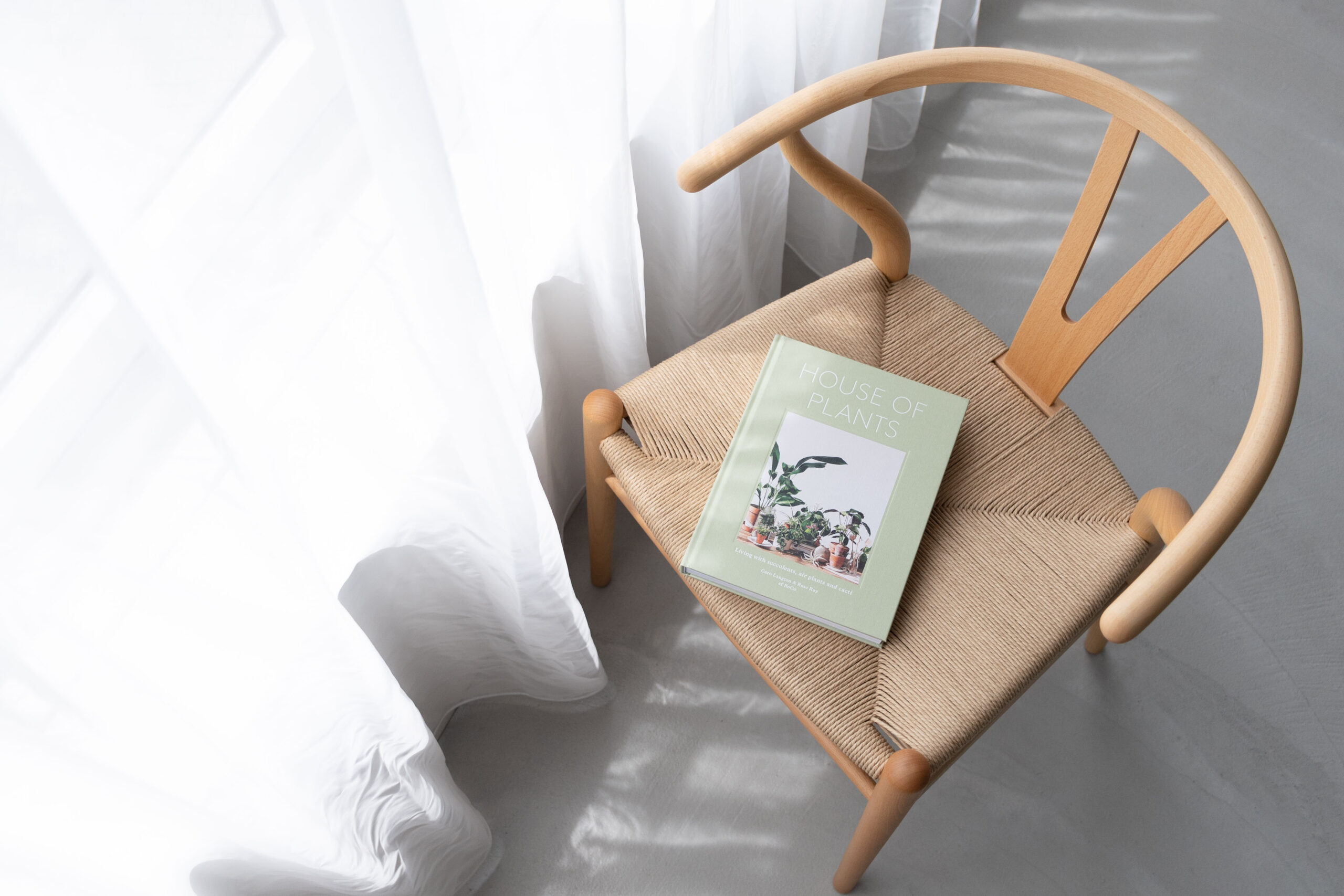 自然光で照らされたカーテンの横に、洋書を置いた椅子がある写真