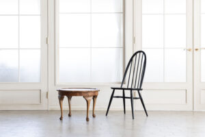 自然光が入る白基調の空間に置かれた、黒い椅子と木製丸テーブルの写真