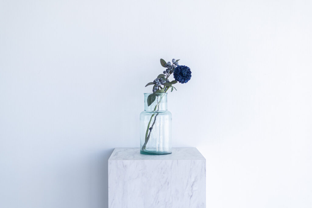 ガラス瓶に入った青い花が、大理石調の台に飾られている写真