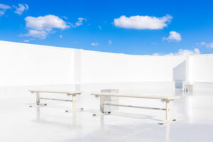 青空の見える屋上に、ベンチが2台並ぶ写真