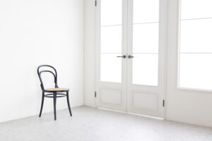 白基調の明るい空間。大きな両開きドア横に1脚の椅子がある写真