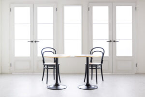 白基調の明るい空間。大きな両開きドア前に並ぶ、黒い椅子とテーブルセット