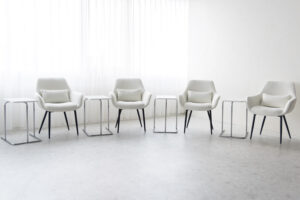 自然光が入る窓際に白い椅子とサイドテーブルが4セット並ぶ写真