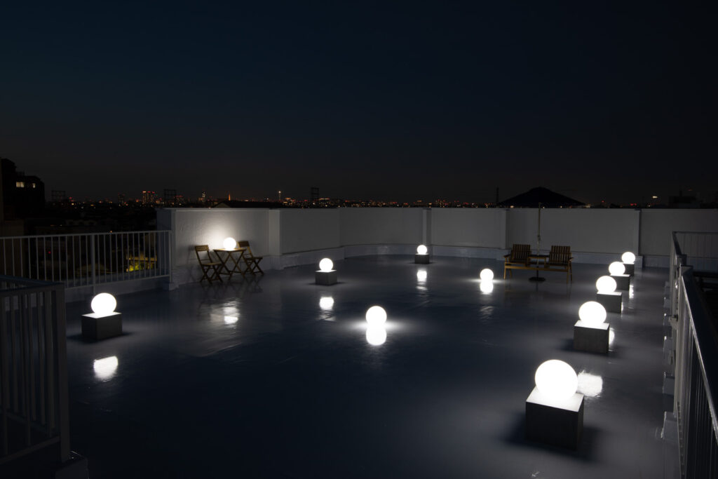 夜間の屋上で、夜景を背景にライティングボールが白く光る写真