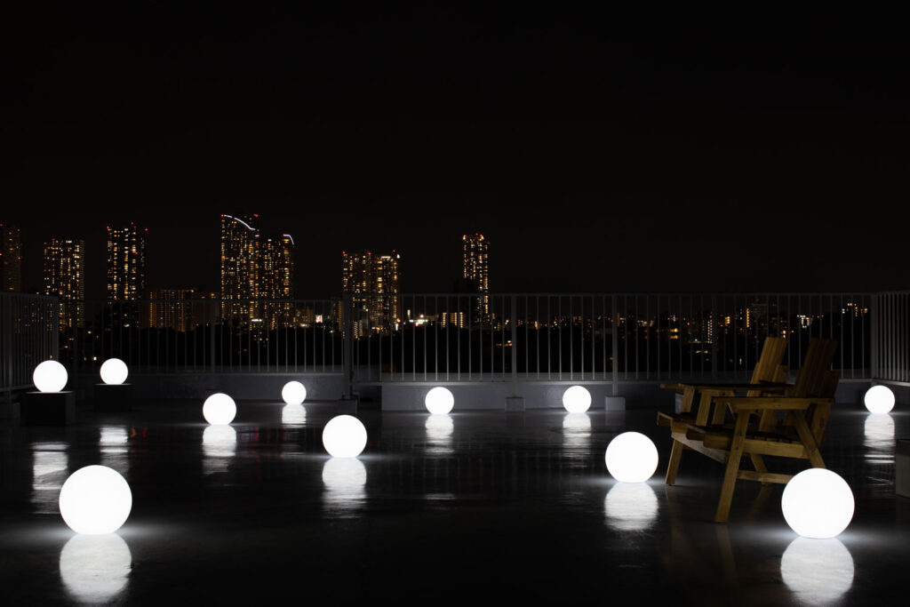 夜間の屋上で、夜景を背景にライティングボールが白く光る写真