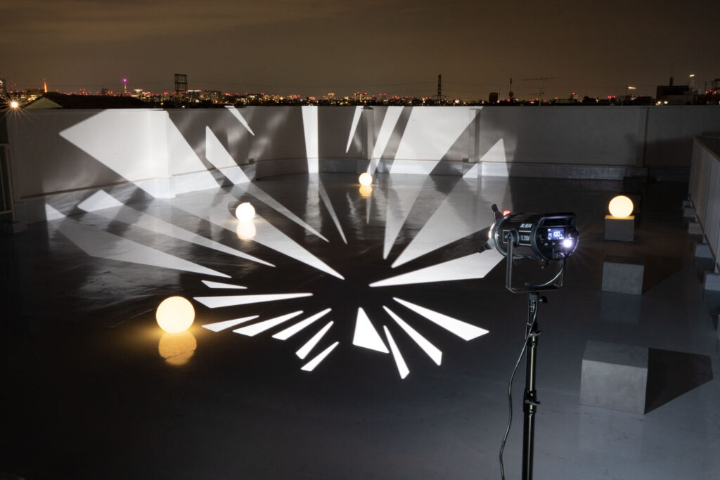 夜間の屋上を、ライトプロジェクターが照らす写真