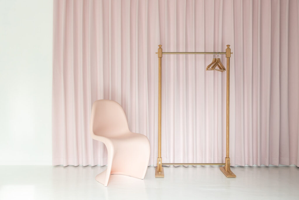 ピンクの壁面カーテン前に、ハンガーラックと椅子が並ぶ写真
