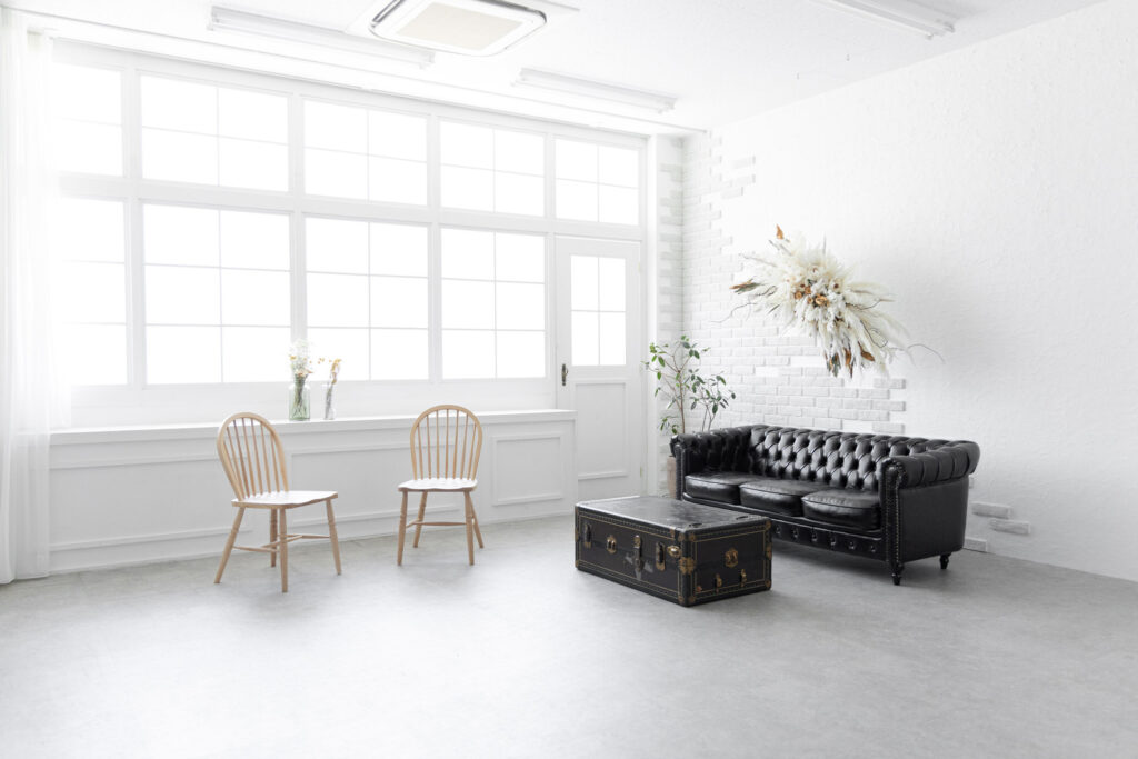 明るい自然光が入る白を基調としたスタジオの写真。黒いソファと木製の椅子がならんでいます。